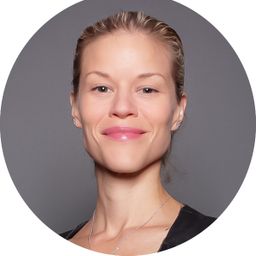 A woman with light blond hair pulled back smiles with closed lips. She wears a black top and delicate necklace. The image is circularly cropped, and the background is a soft gray. Her confident expression and posture convey professionalism.